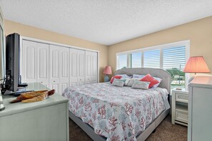 A bedroom with a bed, bedside tables, a desk, a lamp, and a closet. - Direct Beach Views - Sleeps 4, Corner Unit Tennis - Pool (Flagler Beach)