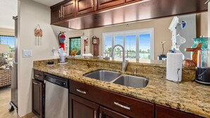 A kitchen with granite countertops, stainless steel sink, and wooden cabinets. - Direct Beach Views - Sleeps 4, Corner Unit Tennis - Pool (Flagler Beach)