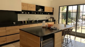 A modern kitchen with wooden cabinets, a black countertop, and a large island with bar stools. - 3 minutes from the center (Provencal village) and shops: Mas St Olive with swimming pool (Maussane-les-Alpilles)