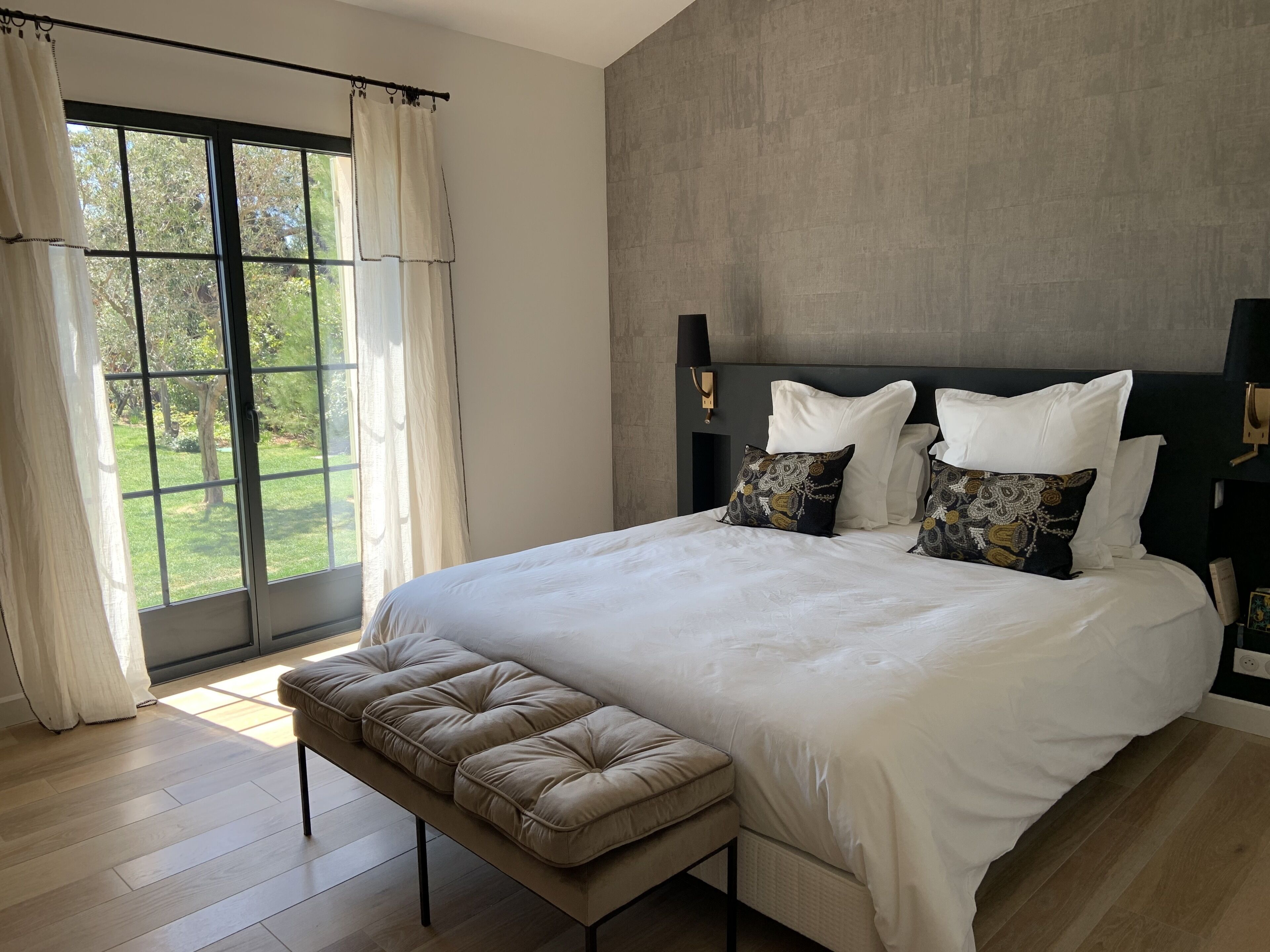 Un dormitorio moderno con una cama grande, un banco y vistas al exterior a través de una ventana.