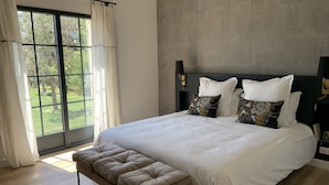 A modern bedroom with a large bed, a bench, and a view of the outdoors through a window. - 3 minutes from the center (Provencal village) and shops: Mas St Olive with swimming pool (Maussane-les-Alpilles)
