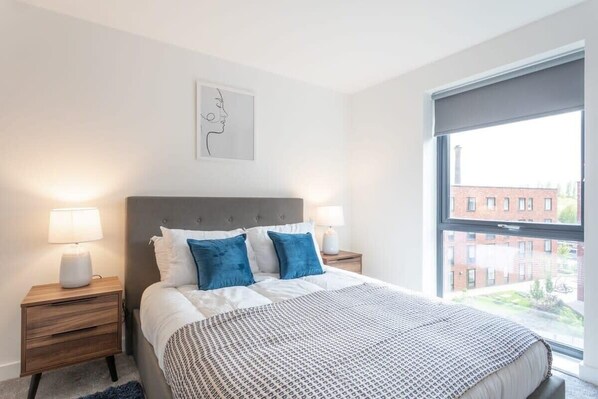 Un dormitorio moderno con una cama grande, dos mesitas de noche y una ventana con vista a la ciudad.