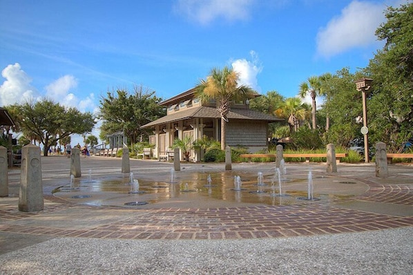 A courtyard with a fountain, a building with a tiled roof, and palm trees.