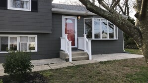 Een woonhuis met twee verdiepingen, een veranda, een kleine boom en een zichtbaar raam.