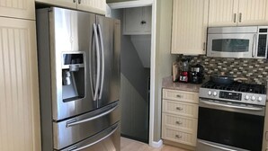 Een keuken met roestvrijstalen apparatuur, waaronder een koelkast, magnetron en kookplaat. Er zijn beige kastjes en een betegelde spatwand.