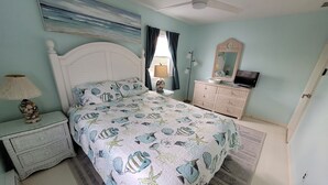 Een slaapkamer met een bed, nachtkastje, kaptafel en een plafondventilator.
