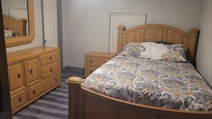A bedroom with a wooden bed, a dresser, a nightstand, a mirror, and a window with blinds. - Spacious Cheerful 1-Bedroom Residential Home (Tulsa)