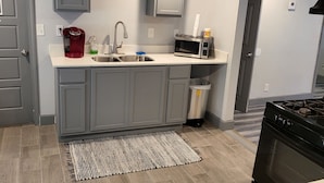 A modern kitchen with grey cabinets, a stainless steel sink, a red coffee maker, a microwave, and a black stove. - Spacious Cheerful 1-Bedroom Residential Home (Tulsa)