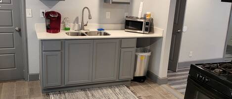 A modern kitchen with grey cabinets, a stainless steel sink, a red coffee maker, a microwave, and a black stove.