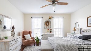 Une chambre à coucher comprenant un lit, une chaise, une commode, une table de chevet, un miroir et un ventilateur de plafond.