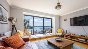 A modern living room with a large window, leather sofa, wooden coffee table, and a TV. - Candle Island View - Harbour Views (Poole)