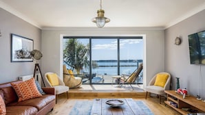 A spacious living room with a leather sofa, a wooden coffee table, and a view of the sea through large windows. - Candle Island View - Harbour Views (Poole)