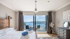 A hotel room with a large bed, a dresser, a fan, and a view of the sea. - Candle Island View - Harbour Views (Poole)