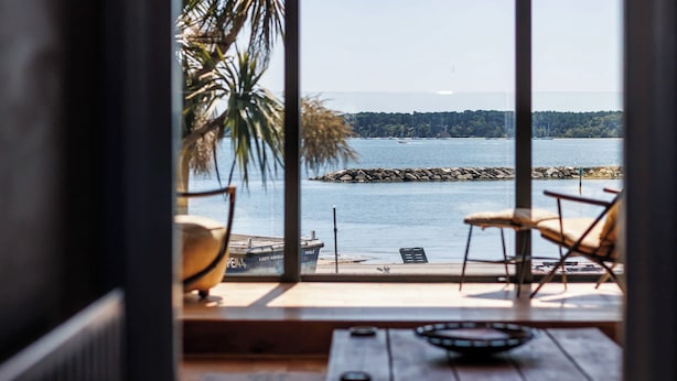 A room with a large window overlooking a body of water, a wooden floor, a ceiling light, and a chair. - Candle Island View - Harbour Views (Poole)