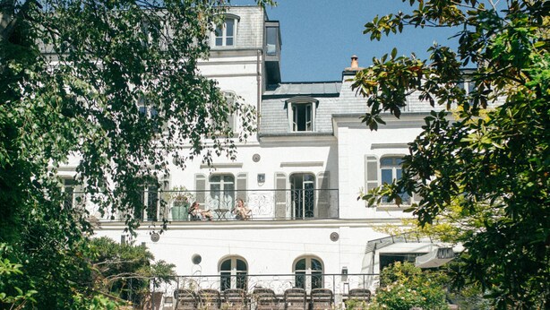 Een historisch gebouw met een bakstenen boog, een balkon en een tuin.