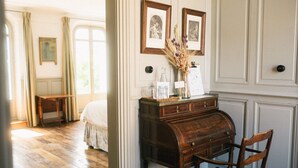 Een slaapkamer met een houten vloer, een bed, een dressoir en een stoel. Boven het dressoir hangen twee foto's in lijsten.