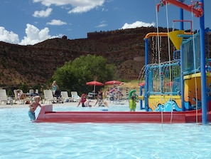A swimming pool with a water play area, lounge chairs, and a mountainous backdrop.