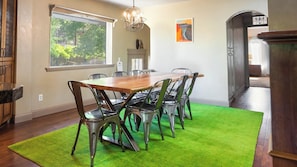 A dining area with a wooden table and metal chairs, a green rug, and a window with a view of greenery.