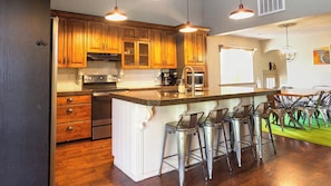 A kitchen with wooden cabinets, stainless steel appliances, a granite countertop, and a bar area with stools.