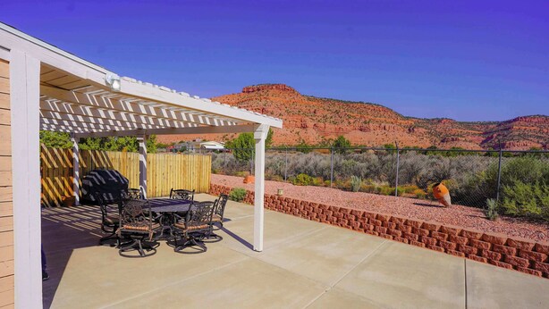 An outdoor patio with a pergola, a table with chairs, and a view of red rock hills. - Vacation Home w/red rock views, Near Zion & Bryce (Kanab)