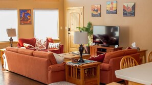 A living room with a sectional sofa, a TV, a lamp, and posters of Bryce Canyon and Zion National Parks. - Vacation Home w/red rock views, Near Zion & Bryce (Kanab)