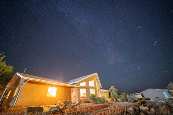 A modern house with a starry night sky, a well-lit entrance, and a landscaped garden.