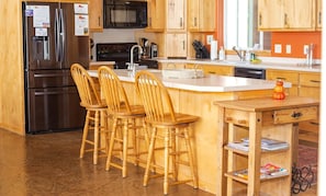 A modern kitchen with wooden cabinets, a stainless steel refrigerator, a built-in oven, and a central island with bar stools.