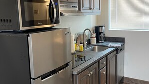 A modern kitchen with stainless steel appliances, wooden cabinets, and a window with blinds. - CORRAL VILLAS<br>Deluxe studios in the north entrance to Yellowstone (Gardiner)