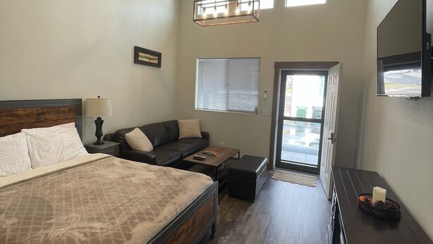 A spacious bedroom with a large bed, a sofa, a desk, and a TV. - CORRAL VILLAS<br>Deluxe studios in the north entrance to Yellowstone (Gardiner)