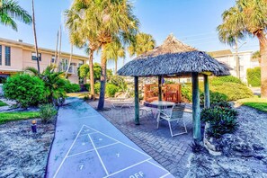 A courtyard with a thatched gazebo, a shuffleboard court, and palm trees.