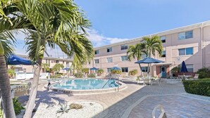 A pool area with lounge chairs, umbrellas, and palm trees.