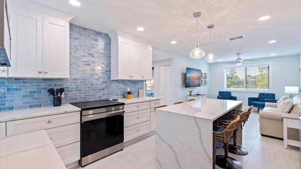 A modern kitchen with white cabinets, a blue-tiled backsplash, and a central island with bar stools.