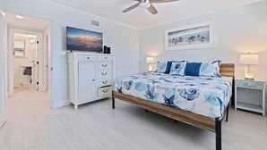 A bedroom with a bed, a ceiling fan, a dresser, a TV, and artwork on the walls.