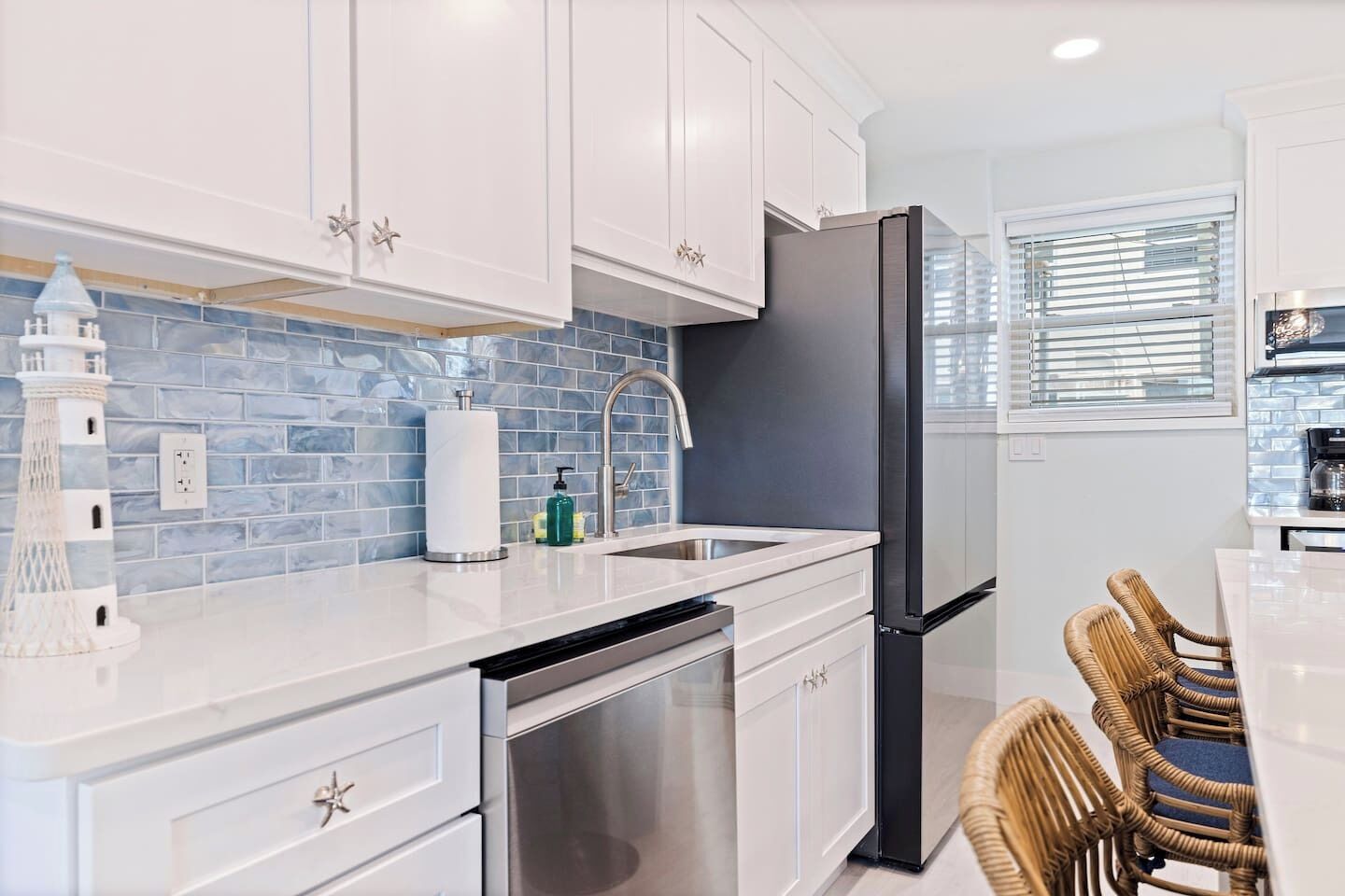 A modern kitchen with white cabinets, a stainless steel refrigerator, a dishwasher, and a sink.