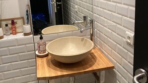 Un bagno con un lavandino grande e rotondo, uno specchio e un piano d'appoggio in legno.