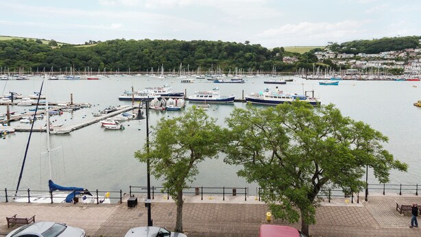 Un port esportiu amb embarcacions amarrades, un passeig per a vianants i una vista d'una població al fons.