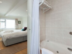 A hotel room with a large bed, a separate bathroom with a bathtub, and a window with curtains. - 2 bedroom accommodation in 8 Lee Court (8 Lee Court)