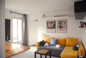 A living room with a yellow sofa, a small table, and two posters on the wall.