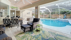 Un patio cubierto con piscina, mobiliario de mimbre y ventilador de techo.
