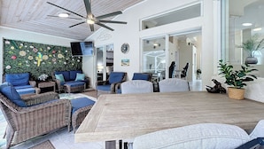 Un amplio espacio de sala con muebles de mimbre, un ventilador de techo y un gran ventanal.