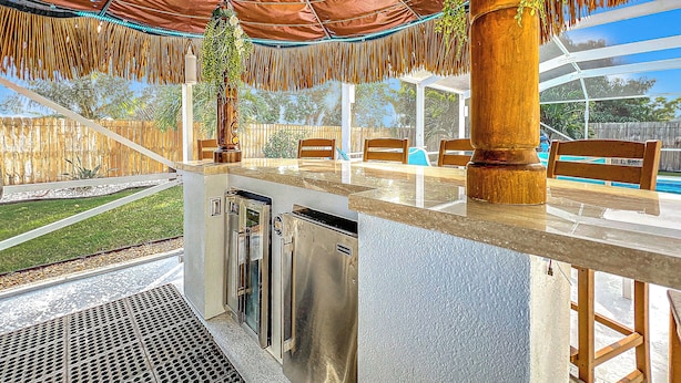Un área de bar al aire libre con barra, asientos y una piscina al fondo.