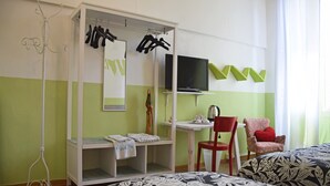 Una habitación de hotel con cama, escritorio, silla, televisor y armario con ropa colgada.