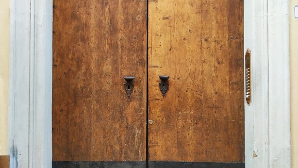 Unas grandes puertas de madera dobles con un pomo de metal, integradas en un arco blanco.