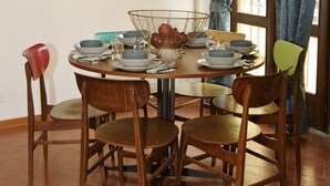 Un comedor con una mesa redonda dispuesta para cuatro personas, rodeada de sillas de madera. Una cesta de alambre se encuentra sobre la mesa, y hay platos y tazones.