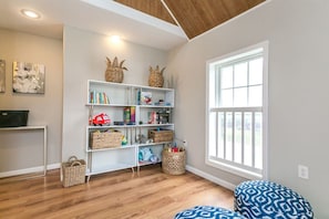 Une pièce avec un plafond en bois, une bibliothèque blanche, une fenêtre et un coussin à motifs.