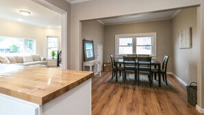 A modern kitchen with a wooden countertop, a dining area with a table and chairs, and a living room with a sofa.