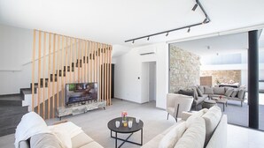 A modern living room with a staircase, a stone wall, and a seating area. - Ayia Napa Kube Villa KB4 -  a villa that sleeps 12 guests  in 5 bedrooms (Ayia Napa)