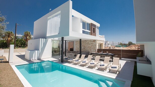 A modern two-story house with a swimming pool, outdoor seating, and a view of the city. - Ayia Napa Kube Villa KB4 -  a villa that sleeps 12 guests  in 5 bedrooms (Ayia Napa)