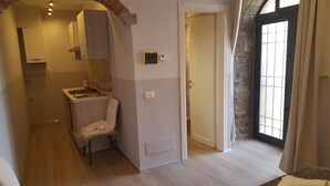 A compact kitchen with a gas stove, a chair, and a small cabinet.
