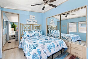 Un dormitorio con cama, ventilador de techo, espejo y ventana con persianas.